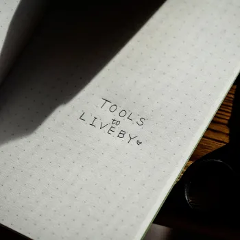interior del cuaderno escrito con las palabras TOOL TO LIVEBY encima de un escritorio de madera oscura
