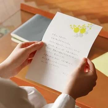 una carta escrita en una hoja con mimosas en las manos de una mujer