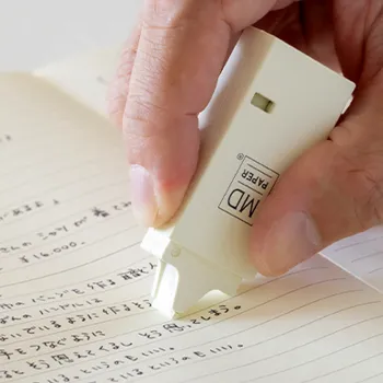 mano de mujer aplicando cinta correctora midori crema sobre cuaderno md rayado