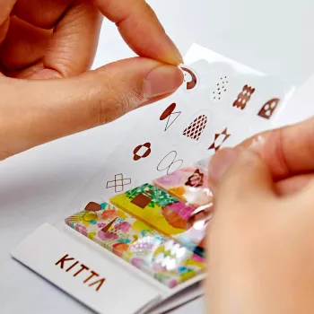hand removing transparent foil stickers from the kitta collage booklet